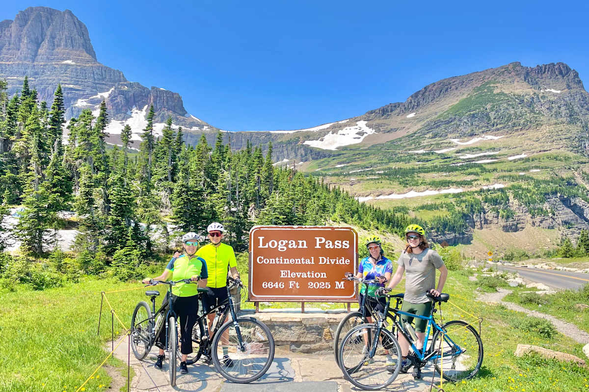 Guests posing with their bikes in front of the Logans Pass sign in Glacier National Park